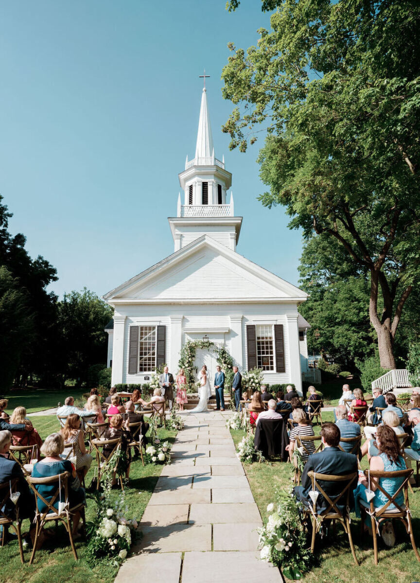 Wedding Aisle: A couple exchanging vows outside a chapel with guests looking on in wooden chairs.