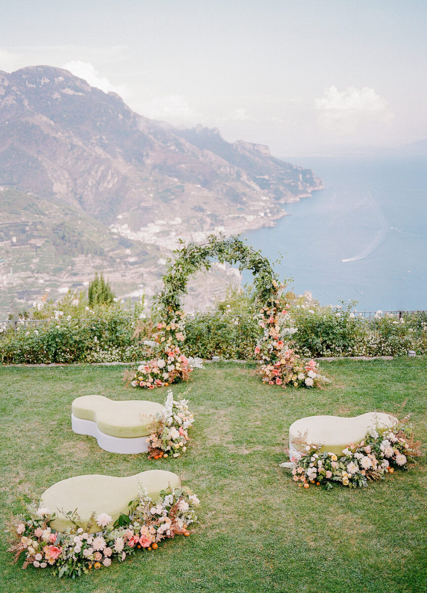 Wedding Aisle: Asymmetrical benches adorned with florals lead up to a ceremony arch overlooking a water view.