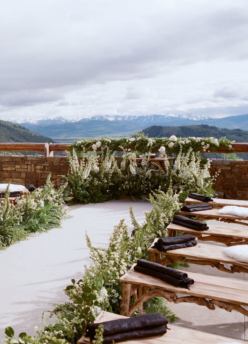 Wedding Aisle: Greenery lining an aisle with wooden benches and blankets in the guest seating section.