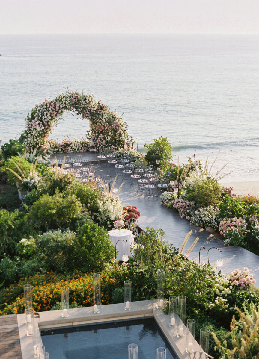 Wedding Aisle: An outdoor ceremony setup by the ocean with lots of greenery and an oversized floral arch.