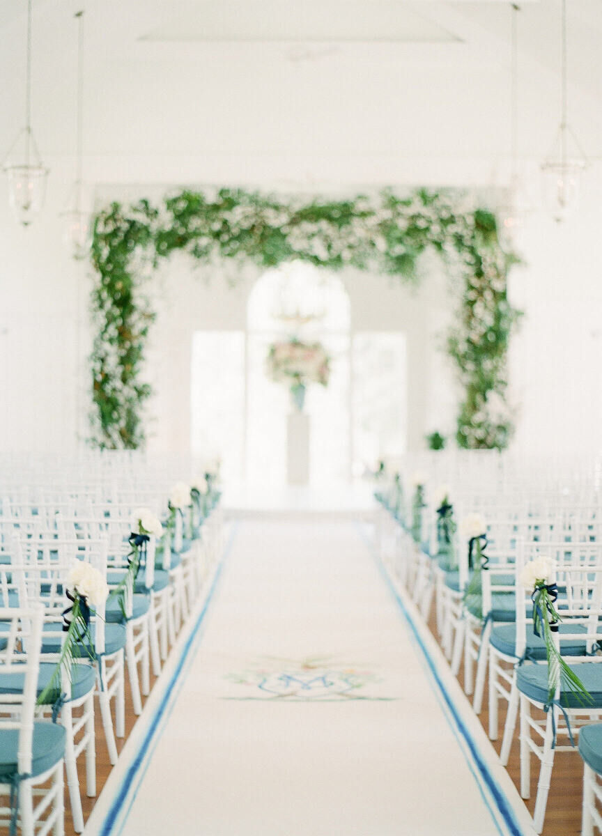 Wedding Aisle: A white runner with a monogram in the center and blue outline, with white and blue-cushioned chairs on either side, all leading up to a wedding altar.