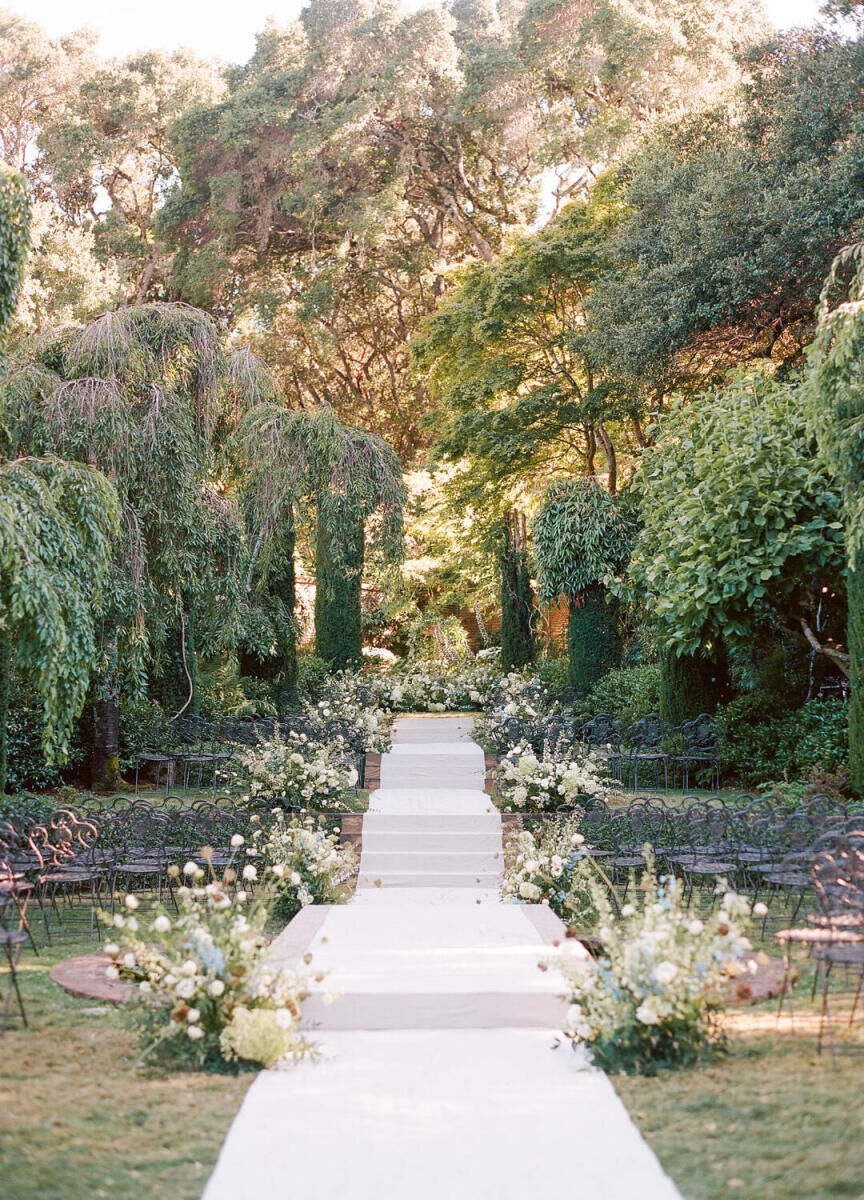 Wedding Aisle: An outdoor ceremony aisle with a runner in a garden setting with floral arrangements on either side.