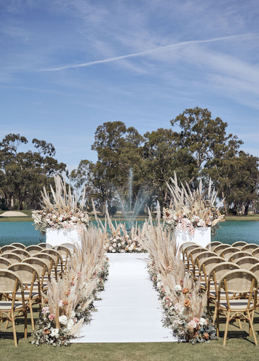 Wedding Aisle: A wedding aisle set-up with pampas grass floral arrangements leading up to a view of the golf course behind it.