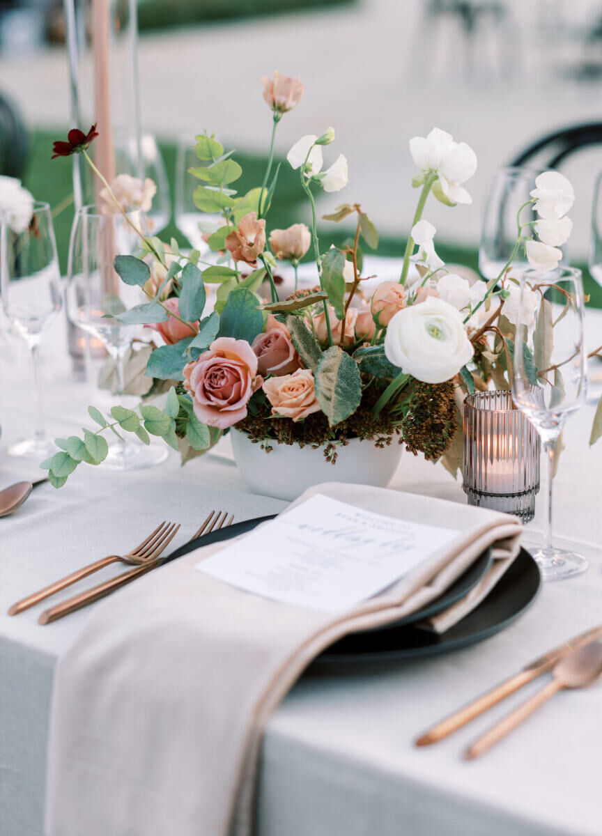 Wedding details: A wedding reception table set with a linen napkin, rose gold silverware, and black plates.