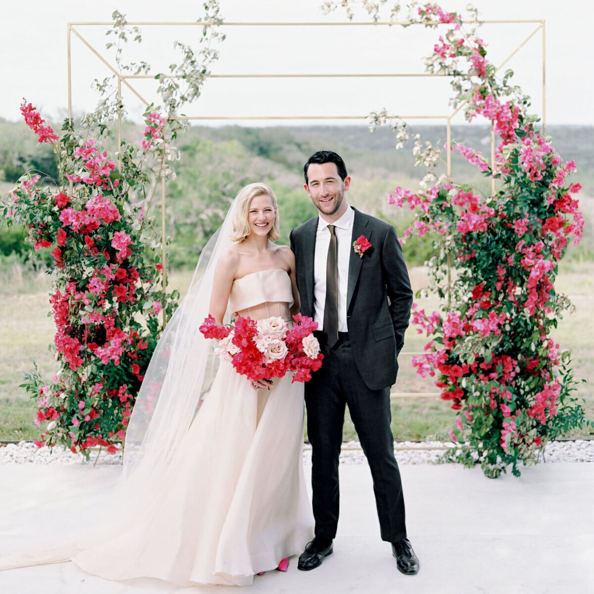 Pink wedding details: A bride and groom standing in their wedding ceremony structure which is covered in pink flowers.