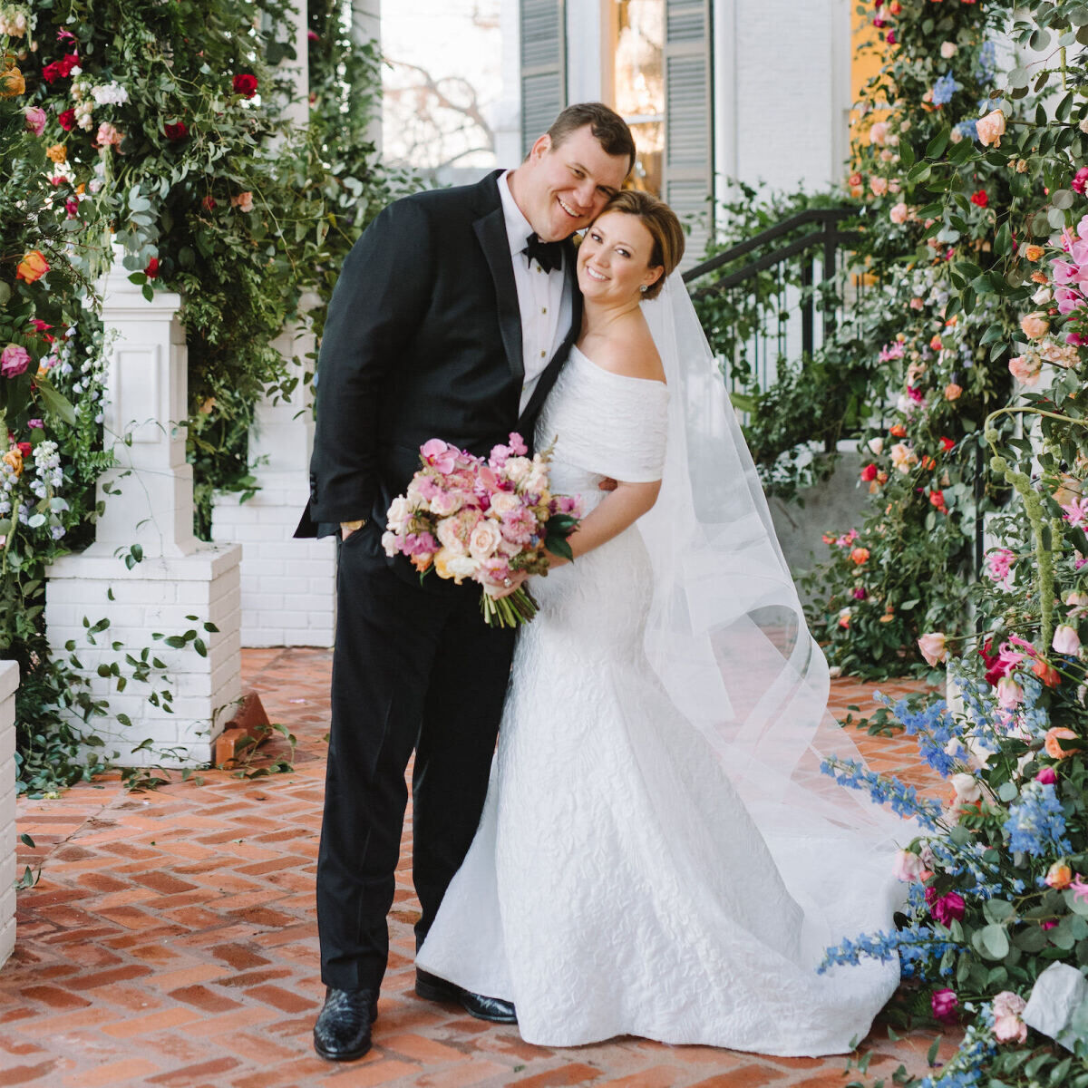 Wedding couple posing under colorful floral wedding arch