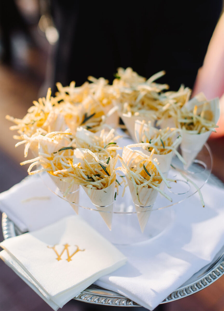 A waiter presents a tray of shoestring fries, served with a monogrammed cocktail napkin.