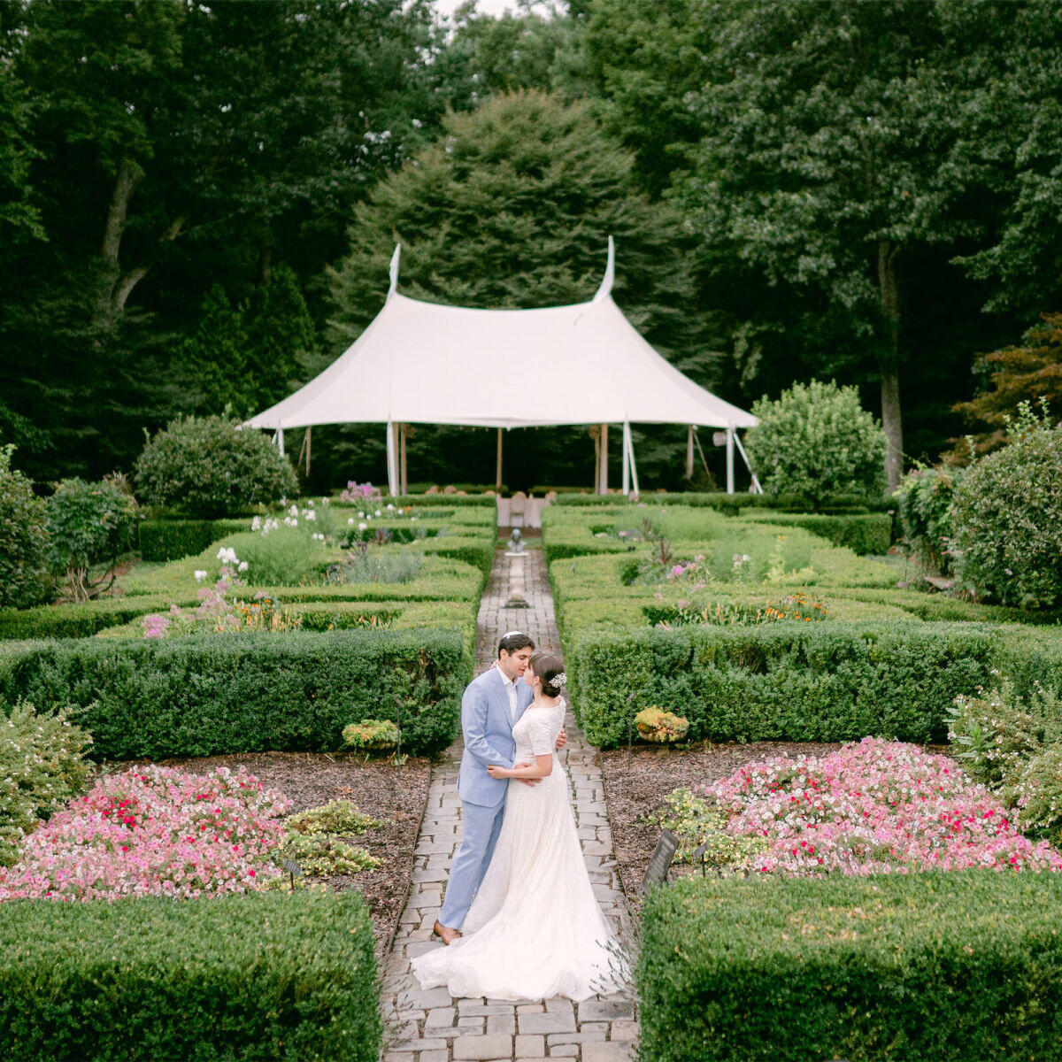 Wedding details: Noa and Adin embracing on the garden path in front of their wedding tent at the Mayflower Inn & Spa in Washington, Connecticut