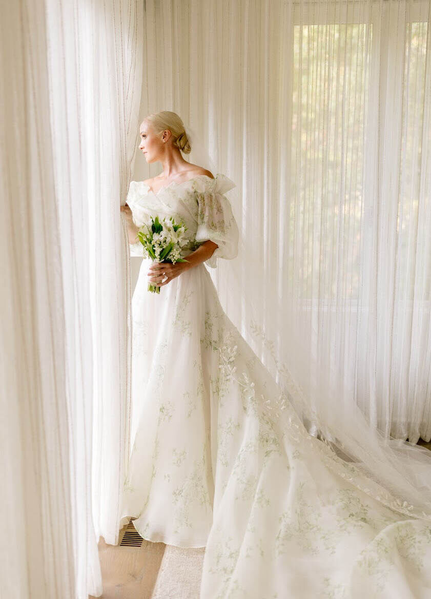 Wedding Dress Shopping: A bride holding a bouquet, wearing an off-the-shoulder patterned wedding gown, looking through a window.