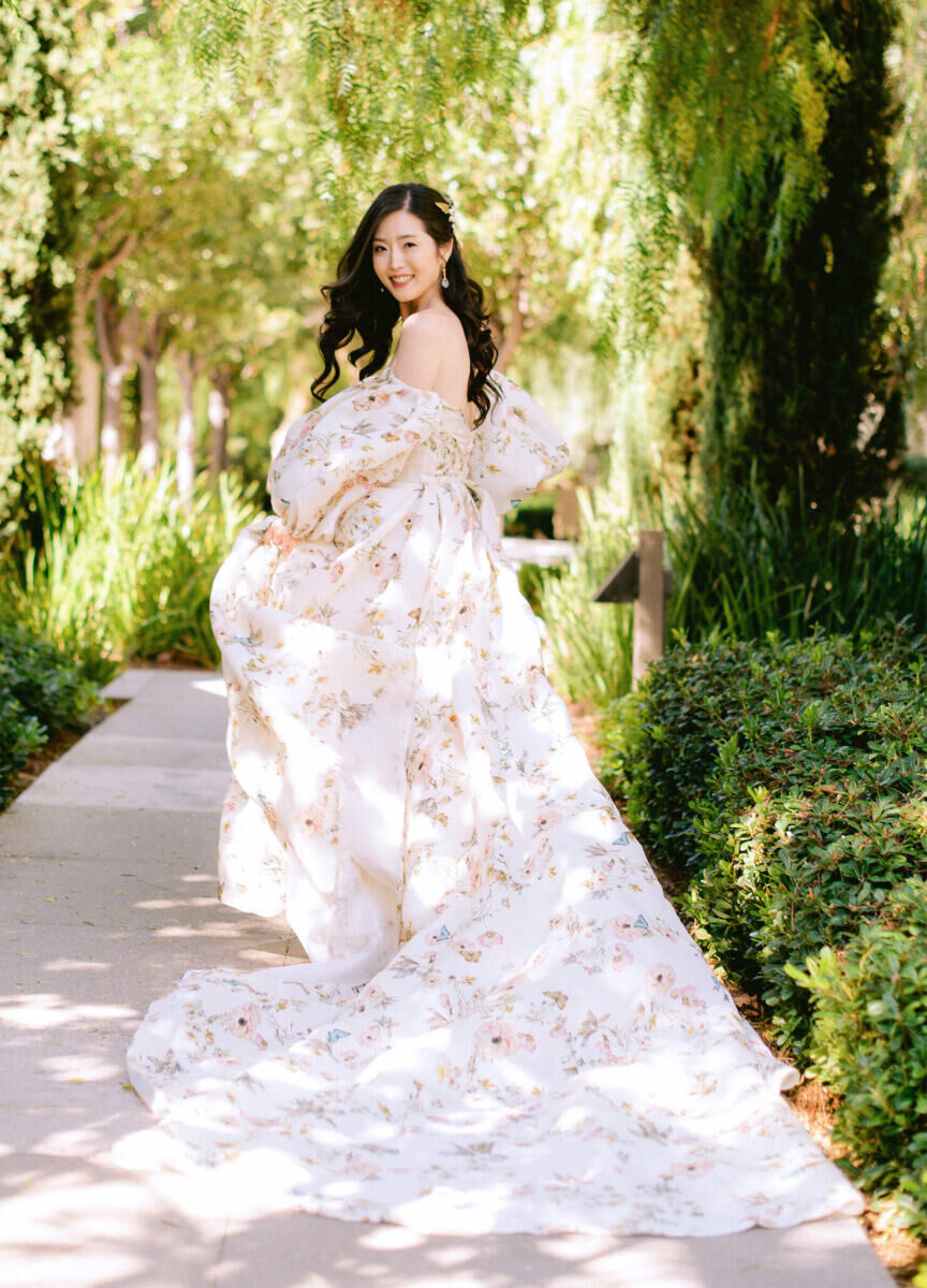 Wedding Dress Shopping: A bride wearing a patterned wedding dress, looking behind her for a photo in a lush garden area.