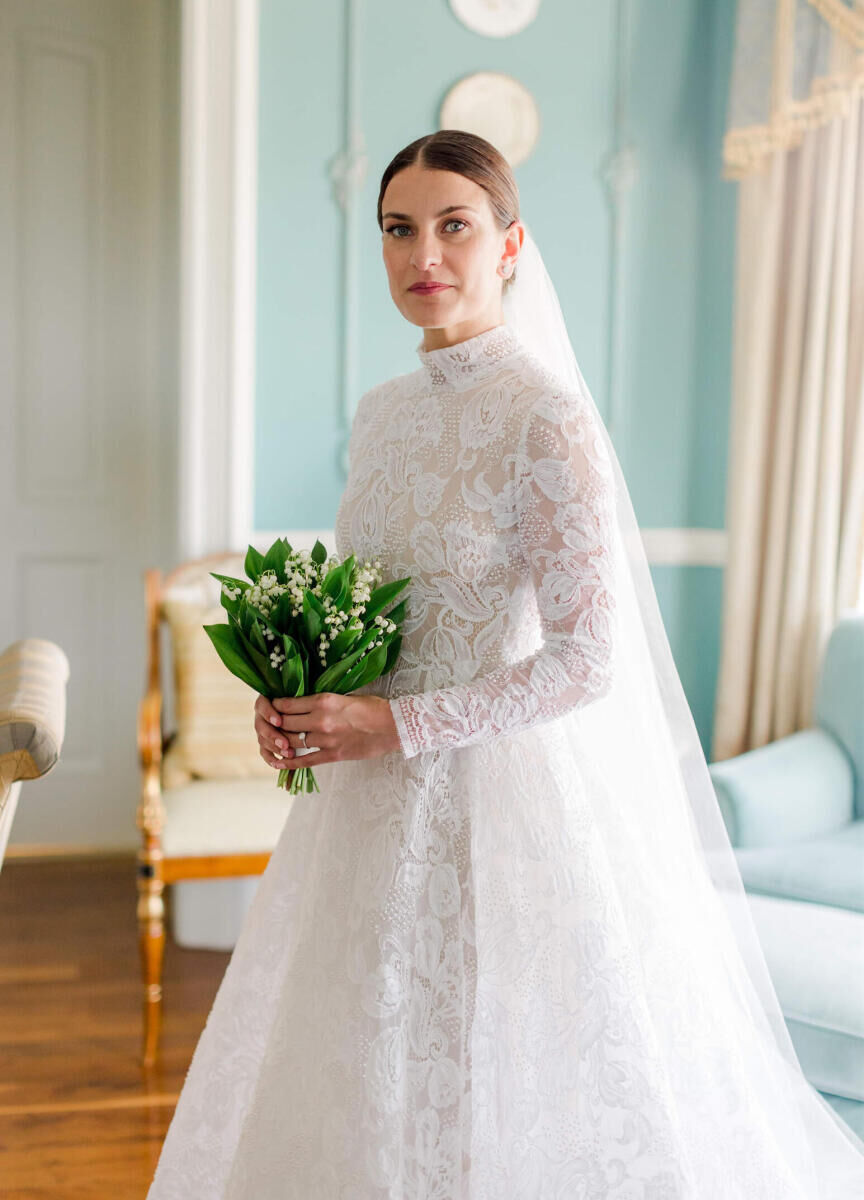 Wedding Dress Shopping: A bride holding a white and green bouquet while wearing a long-sleeve lace wedding gown.