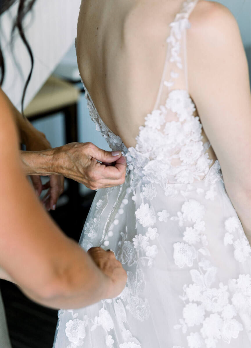 Wedding Dress Shopping: A hand zipping up a bride's sleeveless gown with floral appliques.