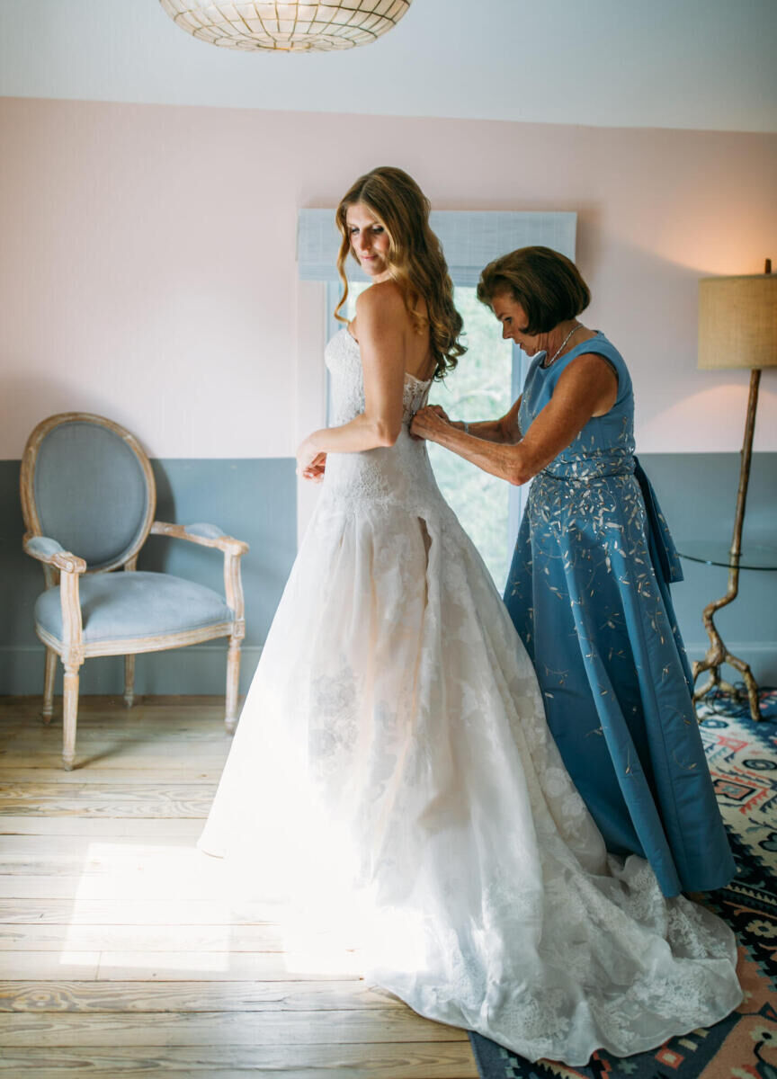 Wedding Dress Shopping: A bride and her mom, who is buttoning up the back of her dress.