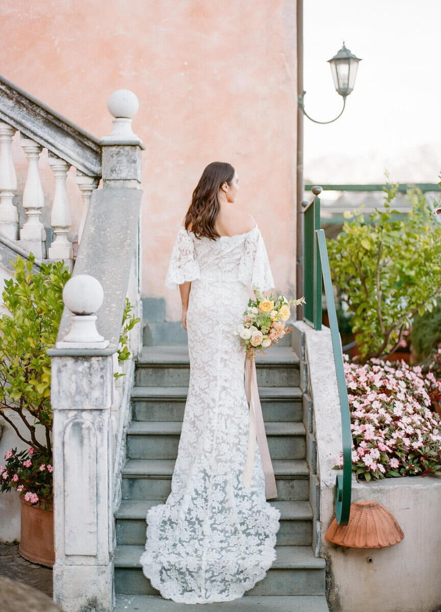 Wedding Dress Shopping: A bride wearing a lace off-the-shoulder gown while holding a multi-colored bouquet and walking up an outdoor staircase.