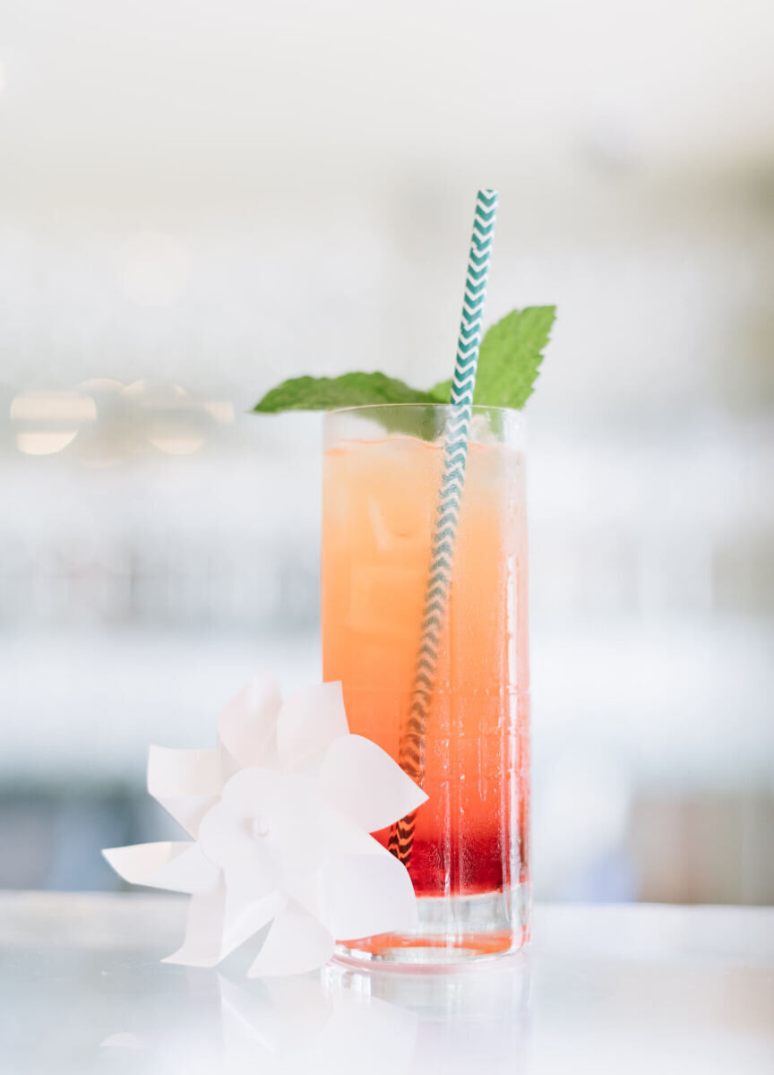 Wedding Drinks: A bourbon and strawberry drink in a tall glass with a straw, mint garnish, and paper flower next to it.