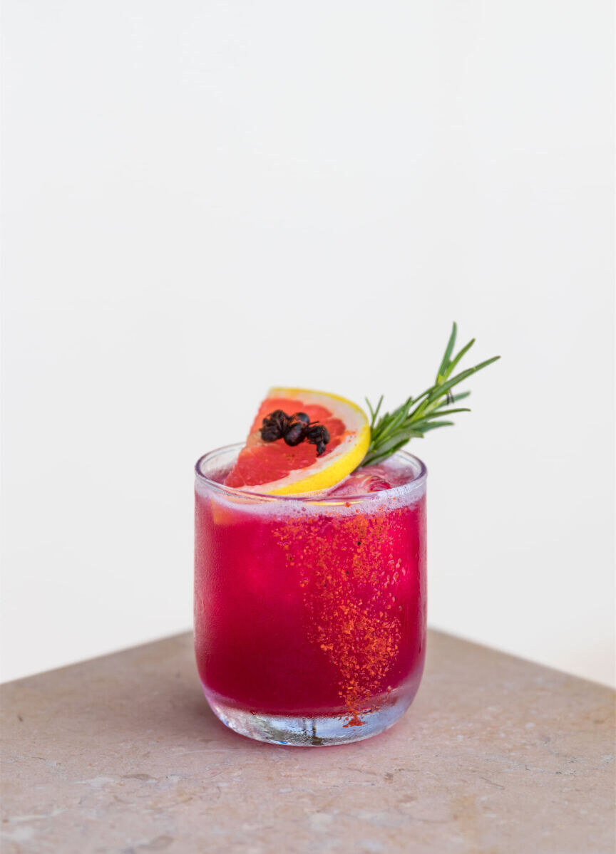 Wedding Drinks: A hot pink cocktail garnished with a rosemary stick, an orange slice, and Chicatana ants.