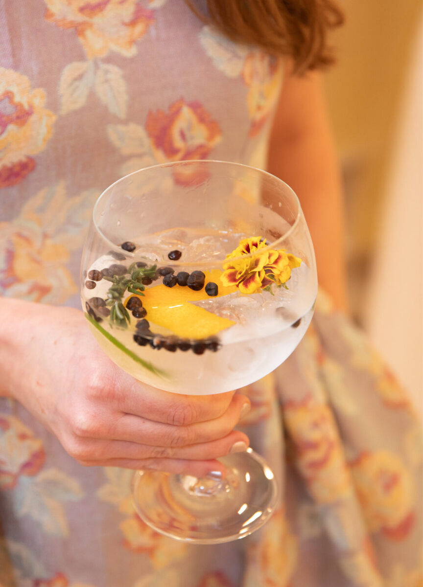 Wedding Drinks: An up-close shot of a woman in a floral dress holding a glass full of a cocktail with several garnishes.