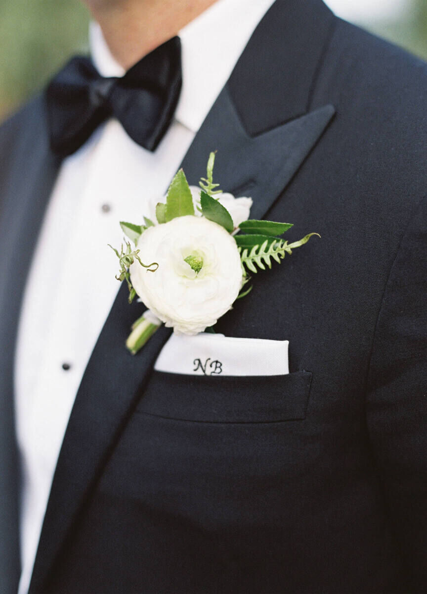 Wedding Etiquette Budget: A groom from the neck-down, wearing a tuxedo with a bow tie, white floral boutonniere, and custom handkerchief.