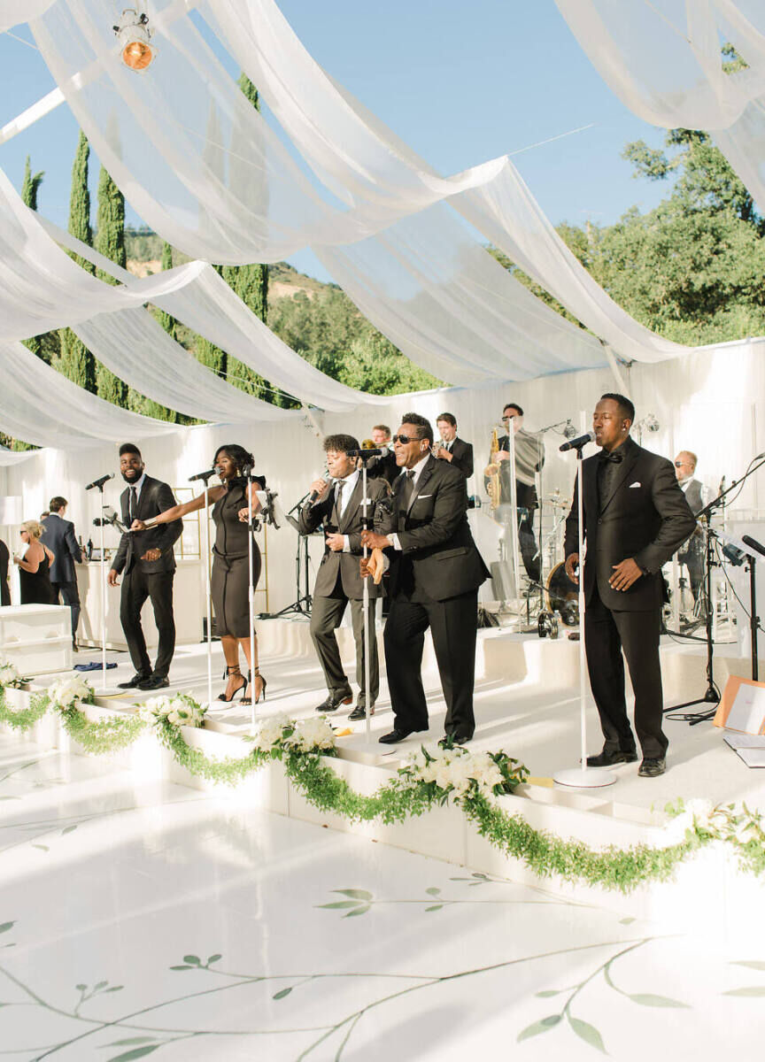 Wedding Etiquette Budget: A band performing on a white stage at an outdoor venue with white fabric hanging from the structure.