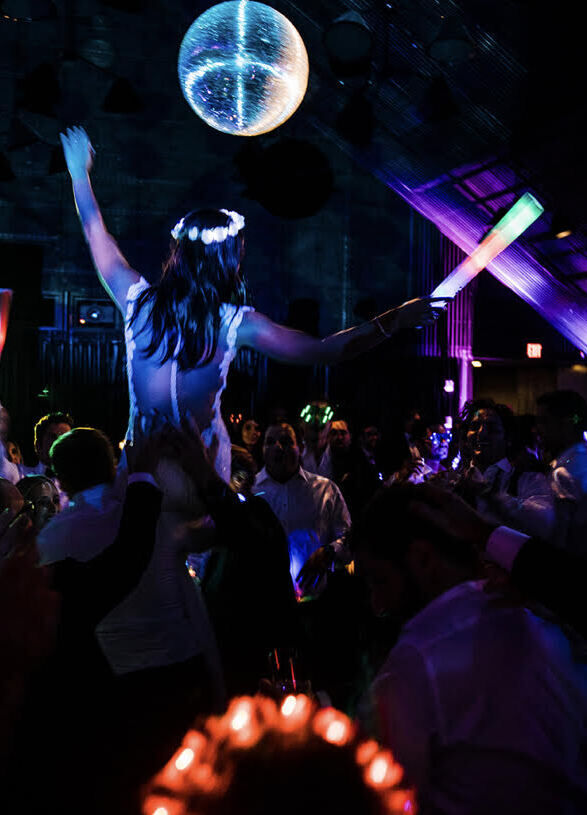 Wedding musician: late-night dj playing at after hours party, guests dancing in the dark with glow wands and a disco ball