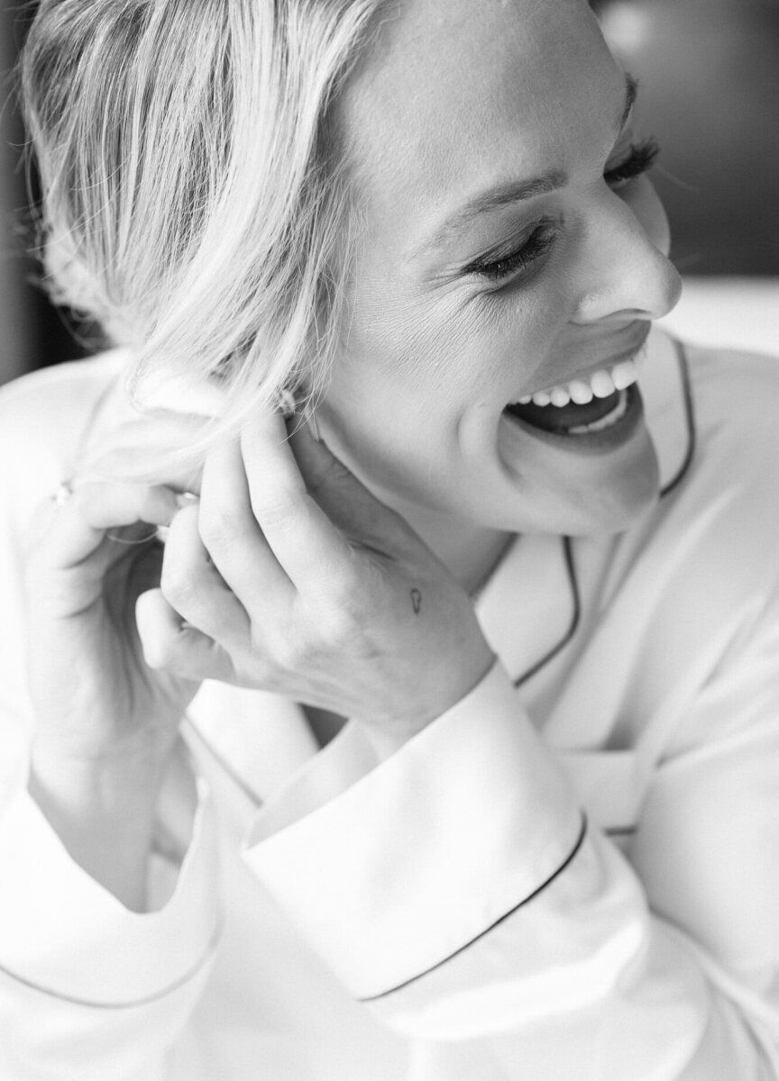 Wedding Photography Ideas: A bride smiling while putting on an earring on her wedding day.