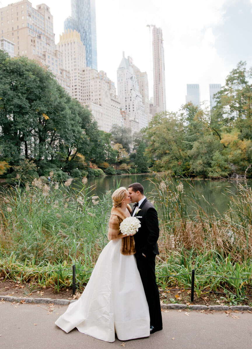 Wedding Photography Ideas: A wedding couple kissing in Central Park, with a pond and skyscrapers in the background.