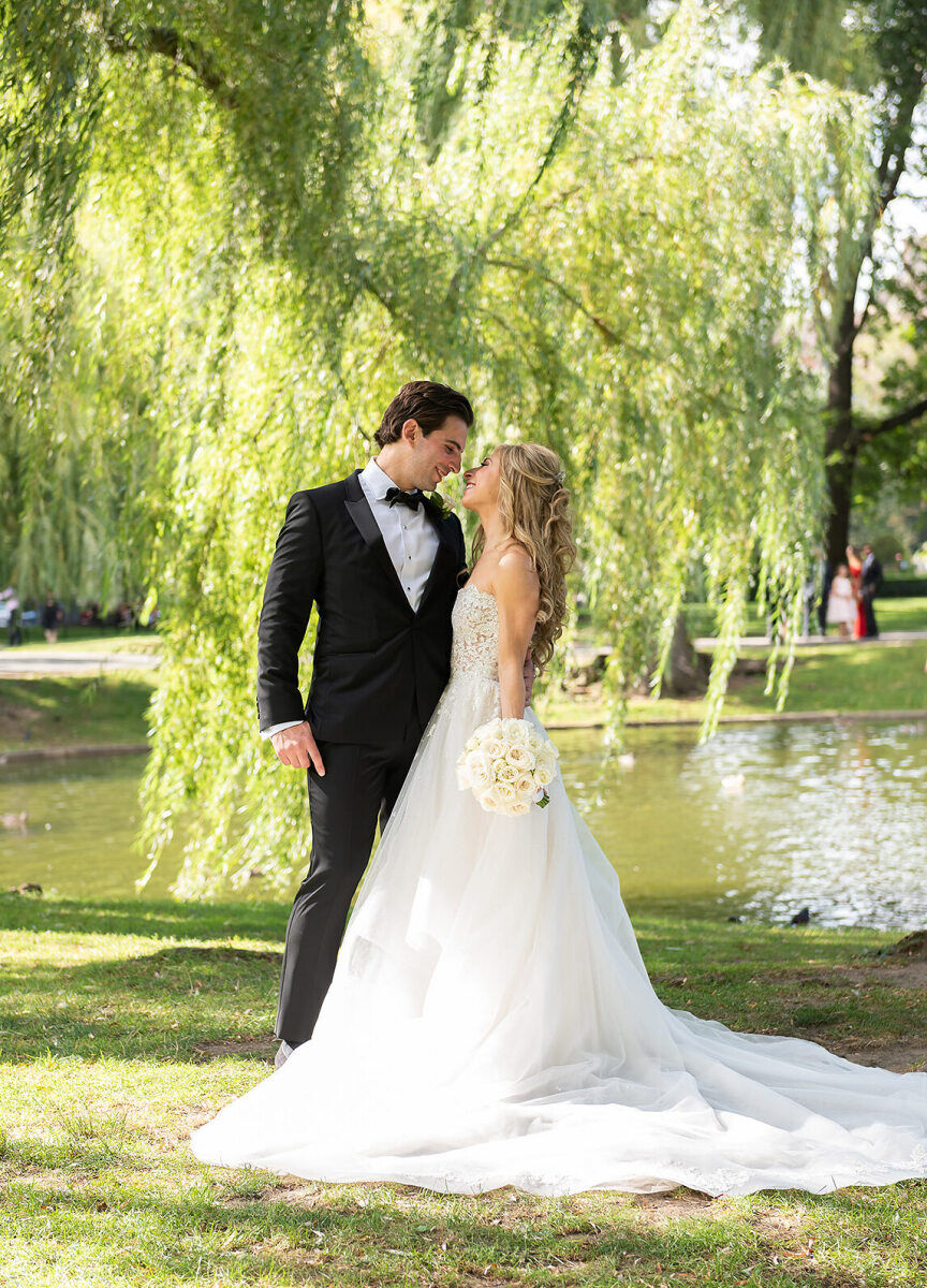 Wedding Photography Ideas: A wedding couple smiling at each other in a portrait, taken in a grassy area overlooking a pond.