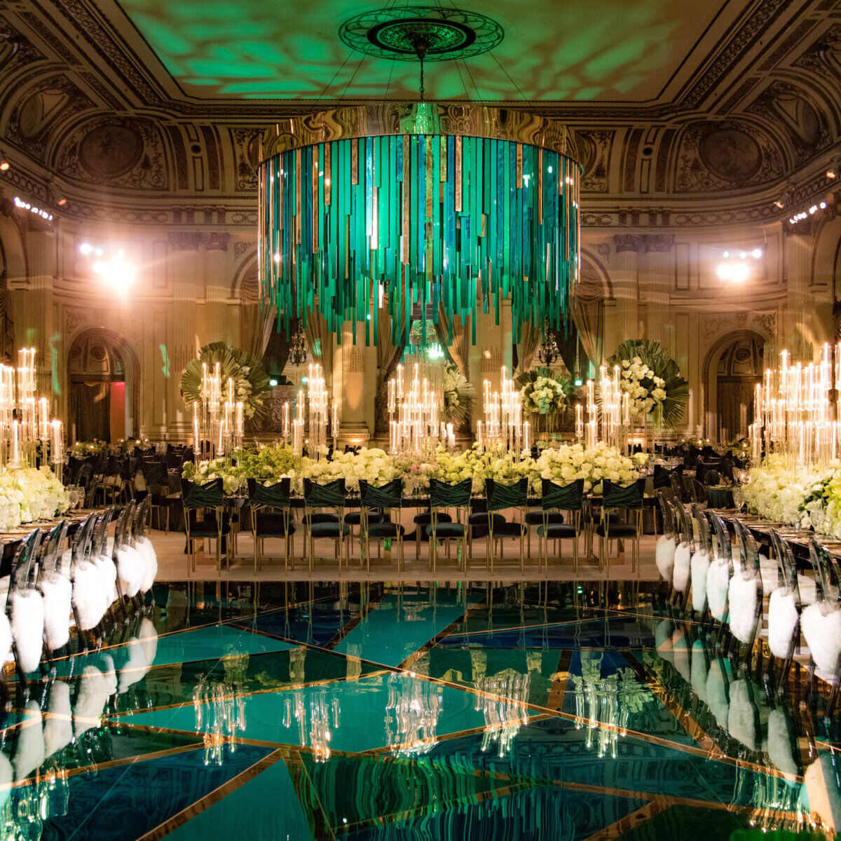 Wedding Planner: Over the top emerald green and gold ballroom wedding ceremony featuring a hanging glass installation over the dance floor