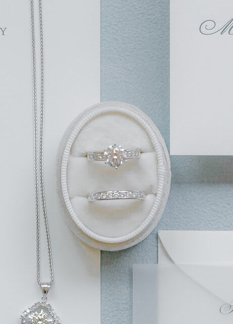 Wedding Ring Design: A Tiffany setting engagement ring in an oval ring box above a wedding band.