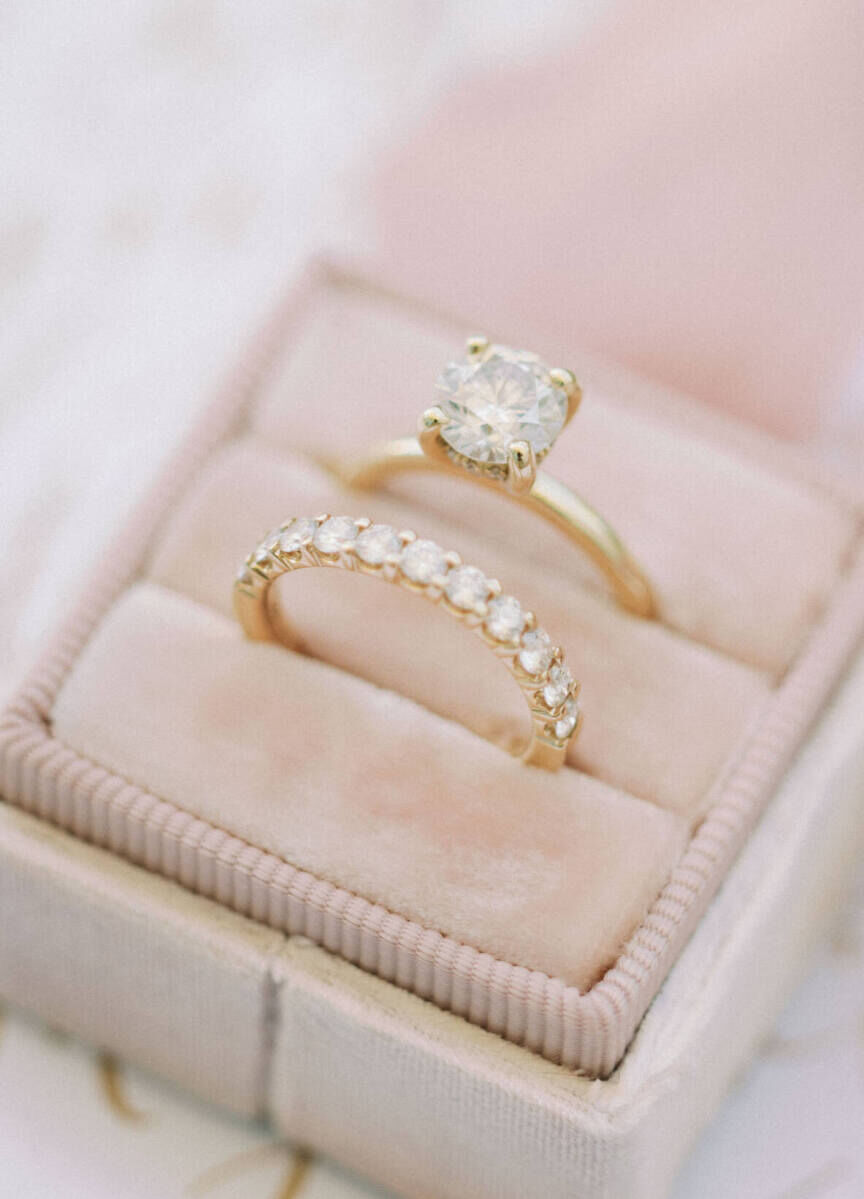 Wedding Ring Design: A gold anniversary wedding ring sitting in a pink ring box next to a solitaire engagement band.