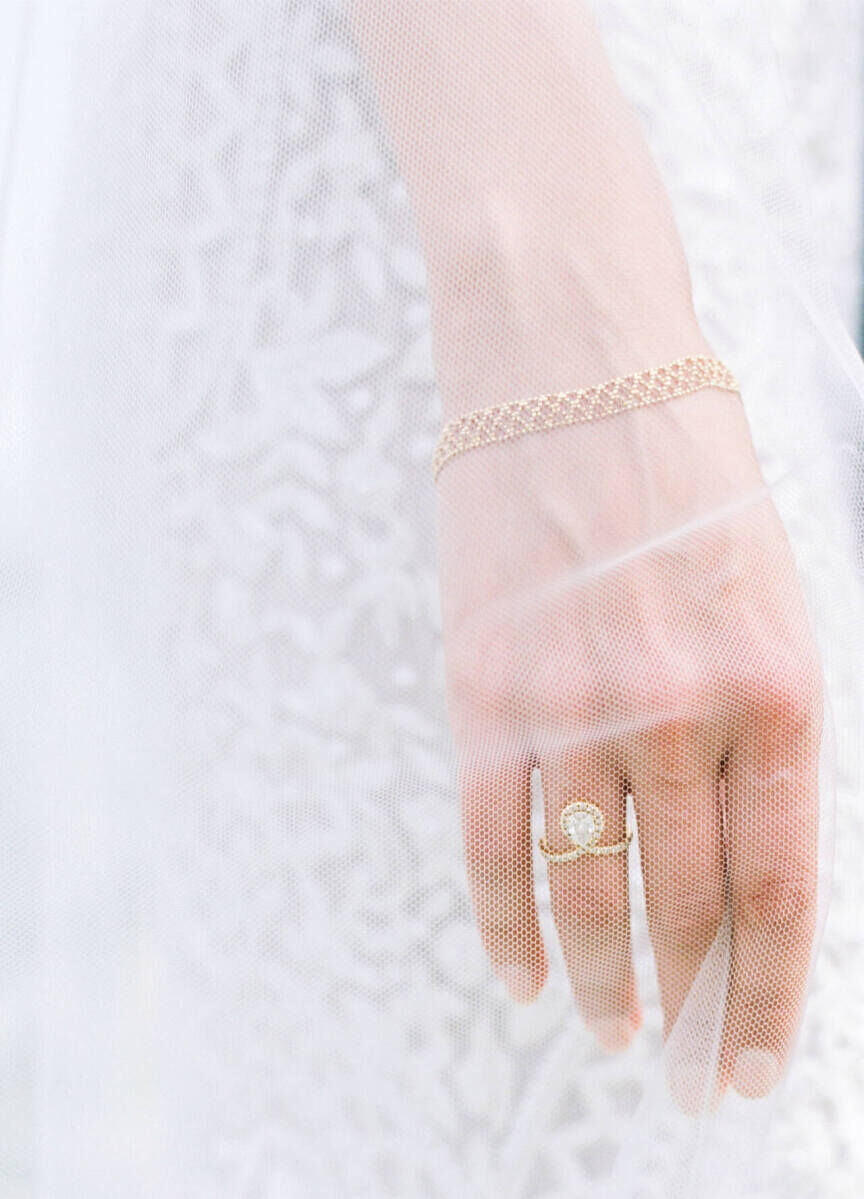 Wedding Ring Design: A bride's hand wearing a pear cut engagement ring seen through her veil.