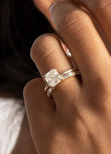 Wedding Ring Design: An asscher cut diamond engagement ring on a ring finger.