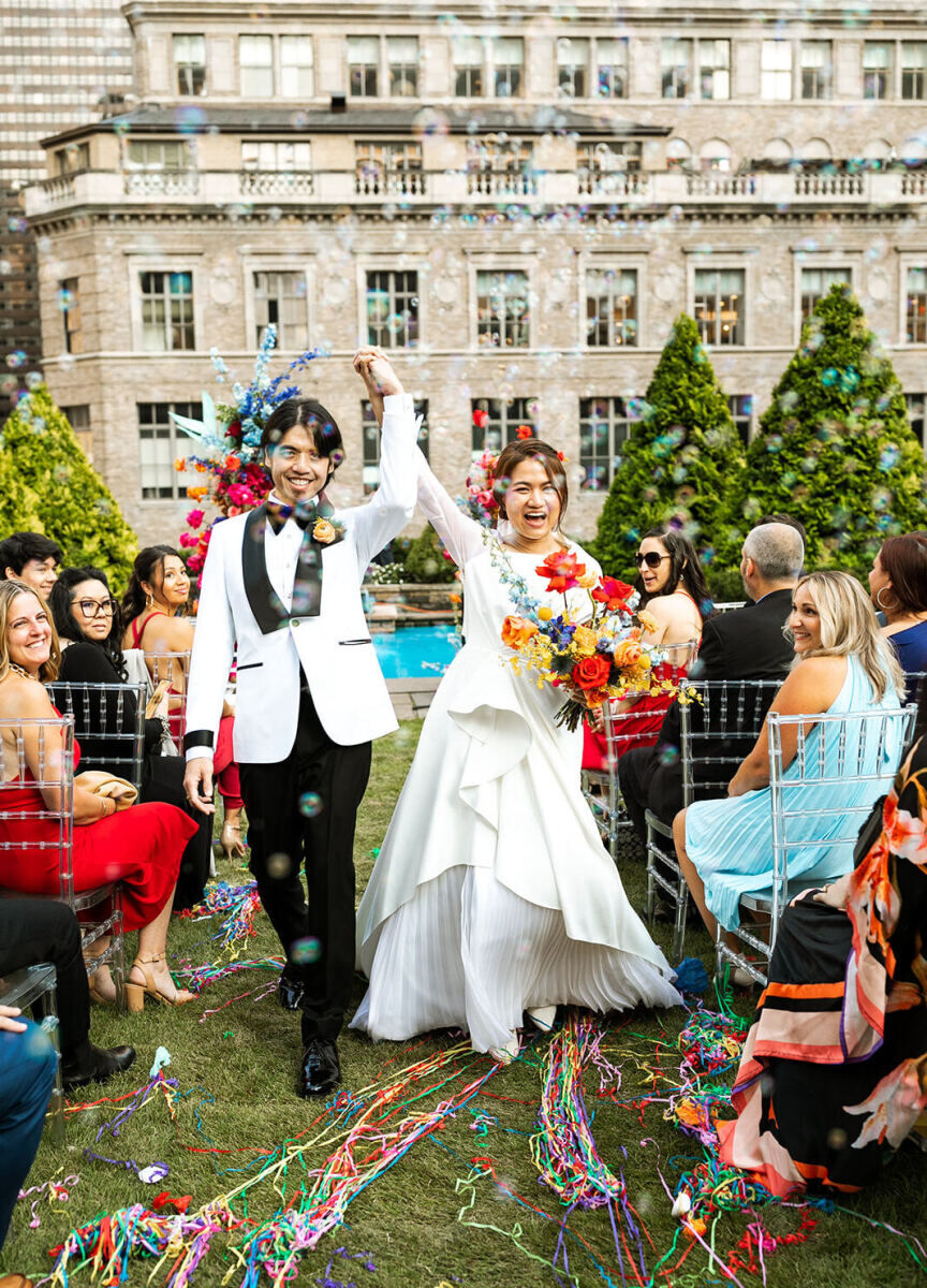 Best Wedding Venues for Creative Couples: A bride and groom walking back down the aisle cheering hand-in-hand at 620 Loft & Garden.