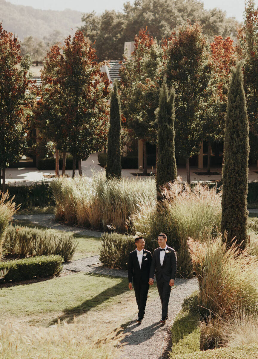 Wedding Venues in California: Two grooms smiling for a candid portrait surrounded by greenery and trees.