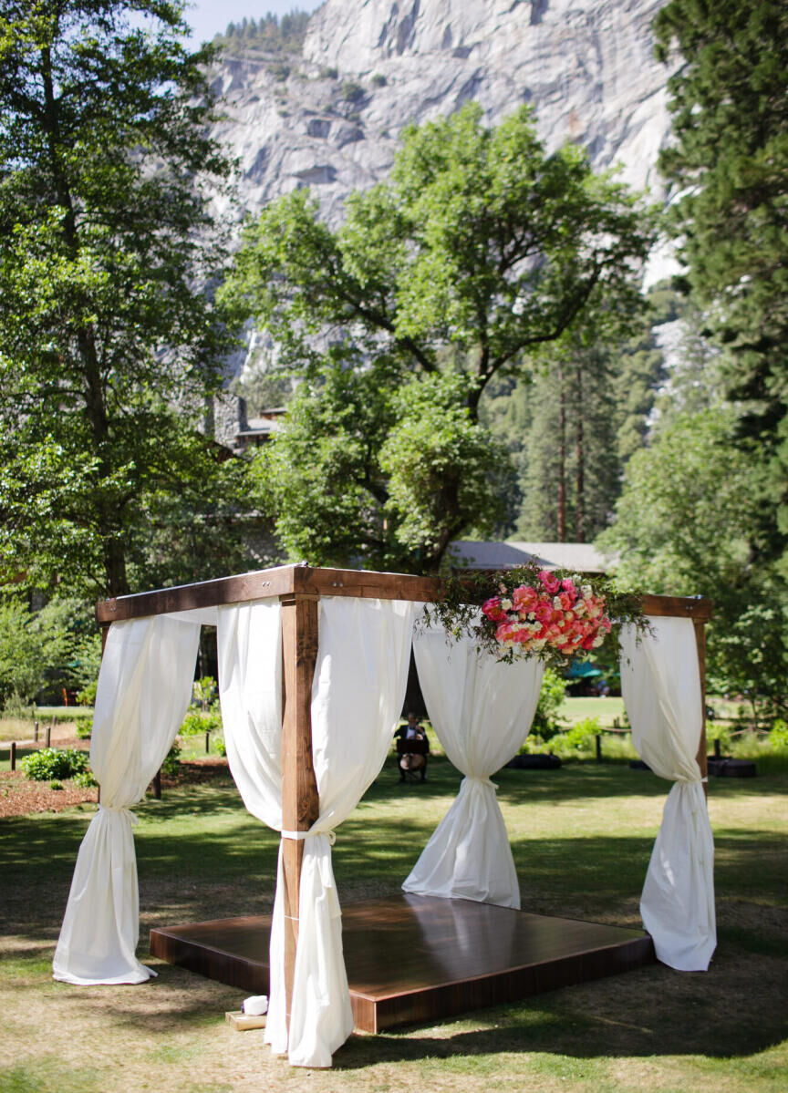 Wedding Venues in California: A wooden gazebo with billowing white fabric with trees and a lodge in the background in Yosemite Valley.