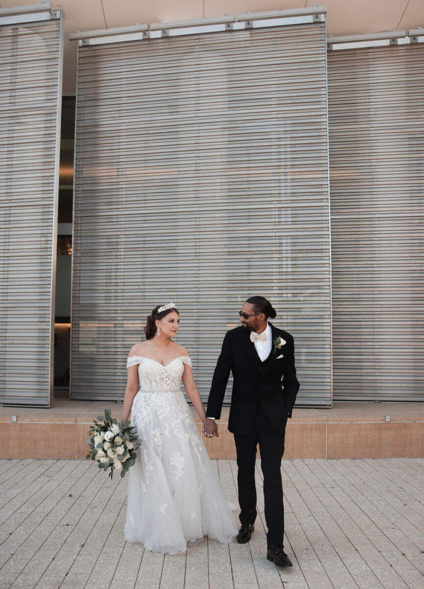 Wedding Venues in California: A bride and groom holding hands outside of a modern outdoor wall in Monterey.