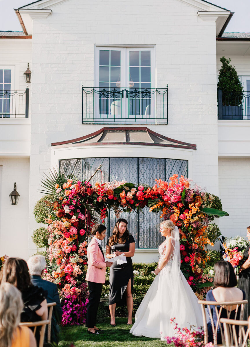 Wedding Venues in California: Two brides looking at each other during their wedding ceremony, complete with a pink and orange floral arch.