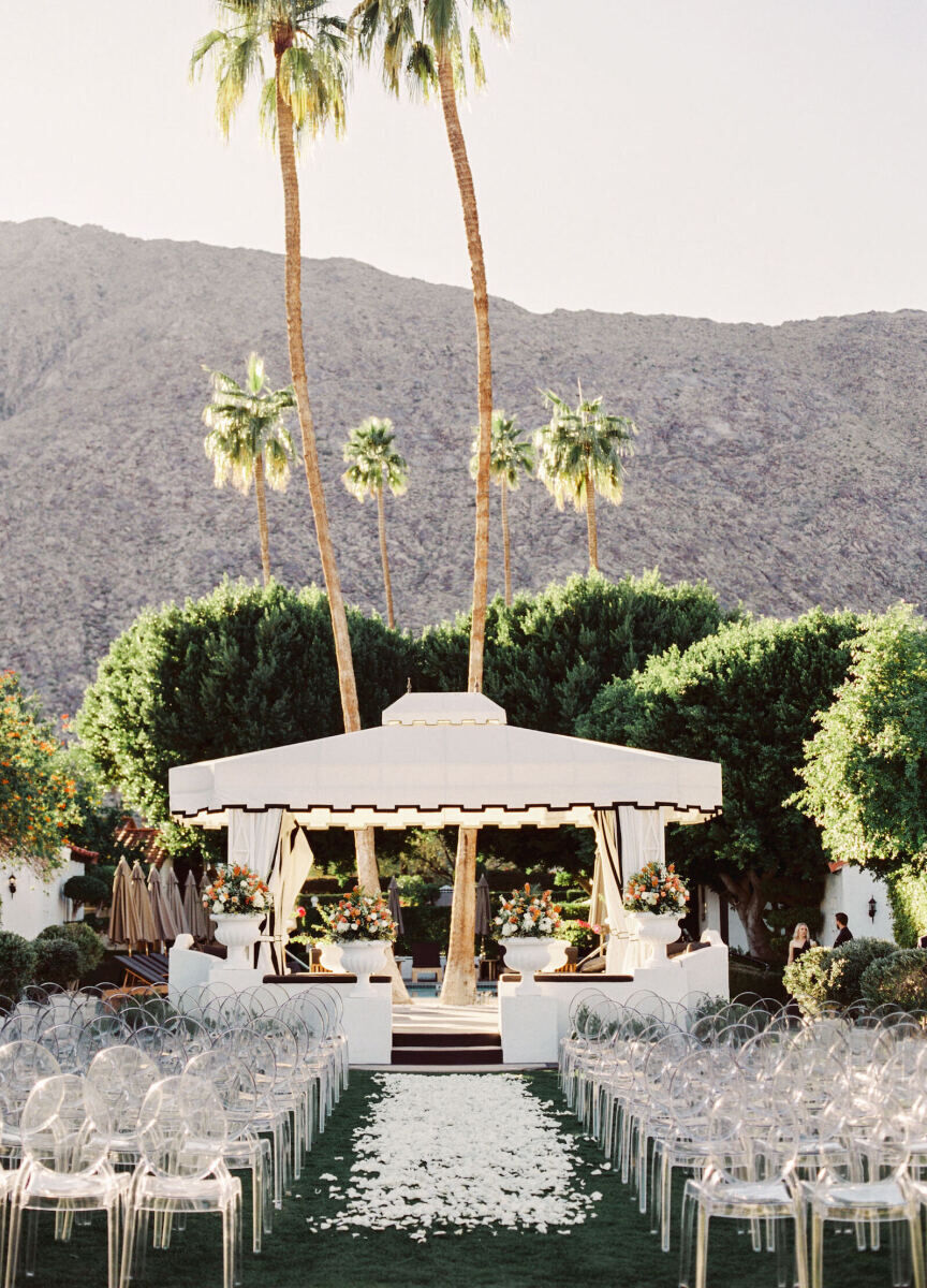 Wedding Venues in California: An outdoor ceremony setup with a cabana at the end of the petal-lined aisle and acrylic chairs on either side.