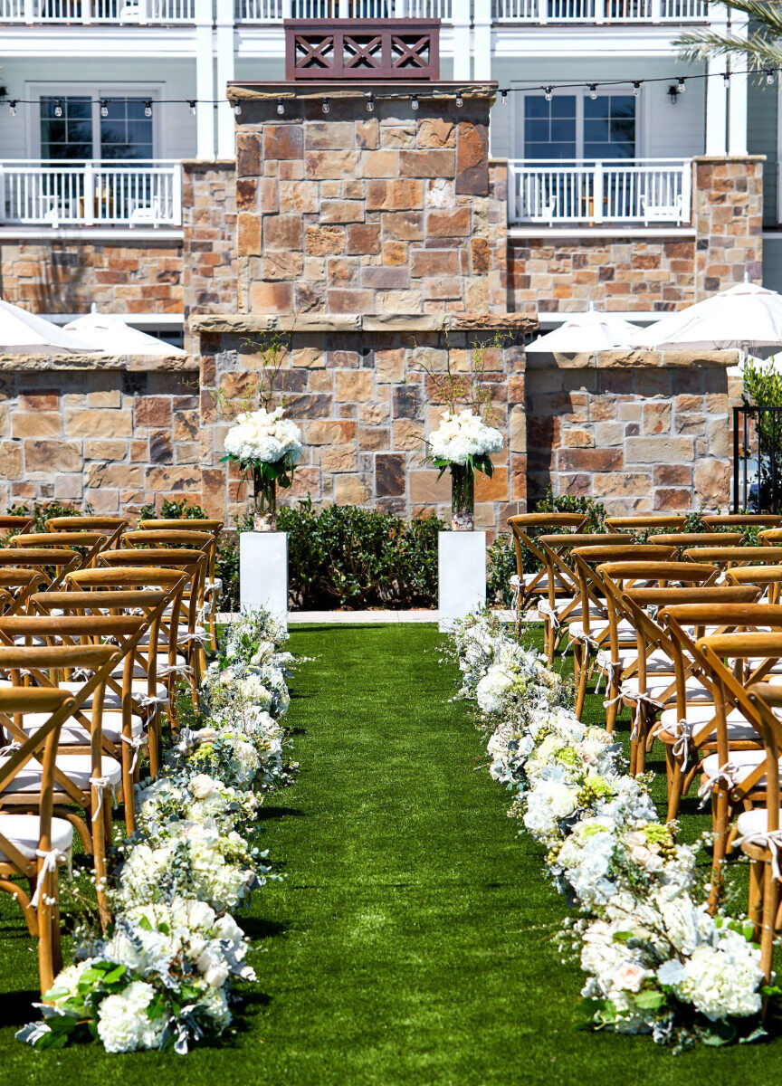 Wedding Venues in California: An outdoor ceremony setup with white cushioned wooden chairs and low-to-the-ground floral arrangements lining the aisle.