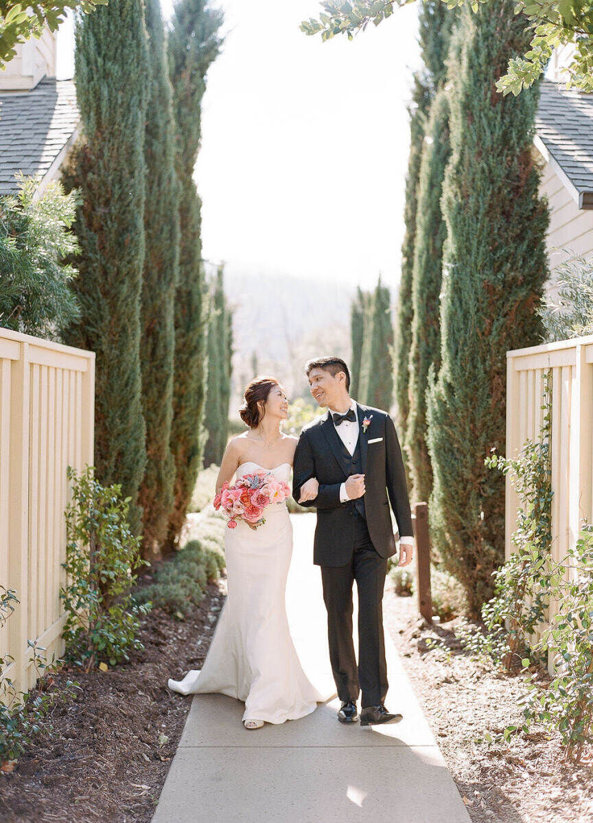 Wedding Venues in California: A bride and groom smiling at each other while walking along a tree-lined pathway.