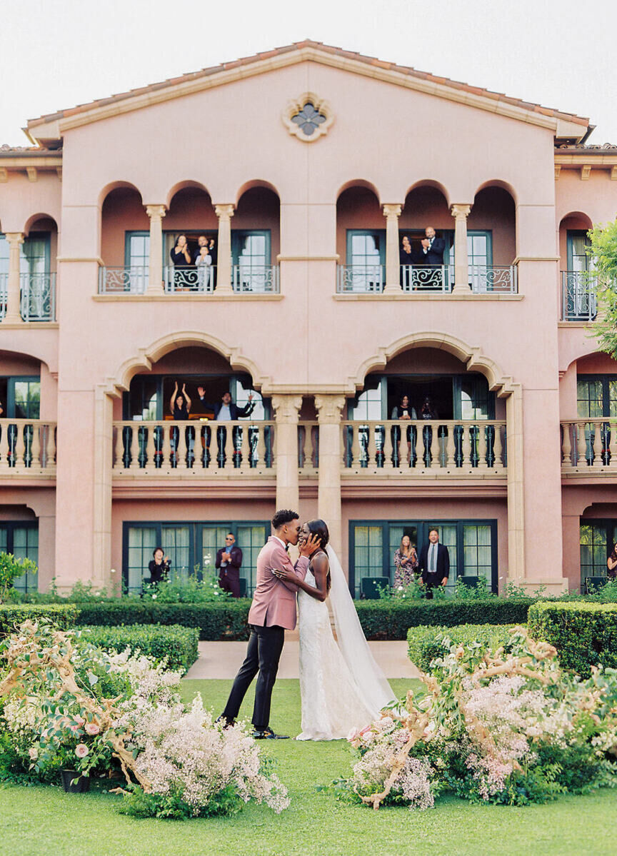 Wedding Venues in California: A bride and groom embracing while their guests look on from a pink hotel in San Diego.