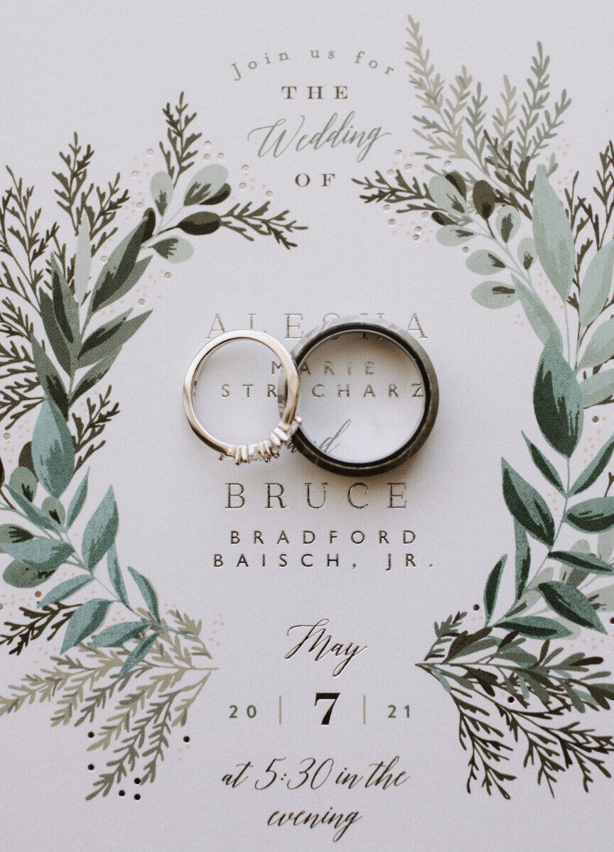 Wedding Website Examples: A flat lay of a bride and groom's rings on top of their wedding invitation.