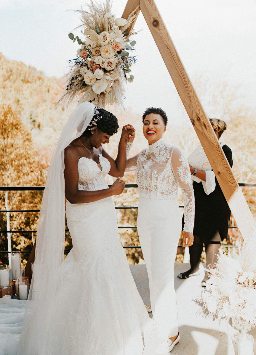 Wedding Website Examples: A wedding couple celebrating at their outdoor wedding ceremony, complete with a triangle-shaped wooden archway.