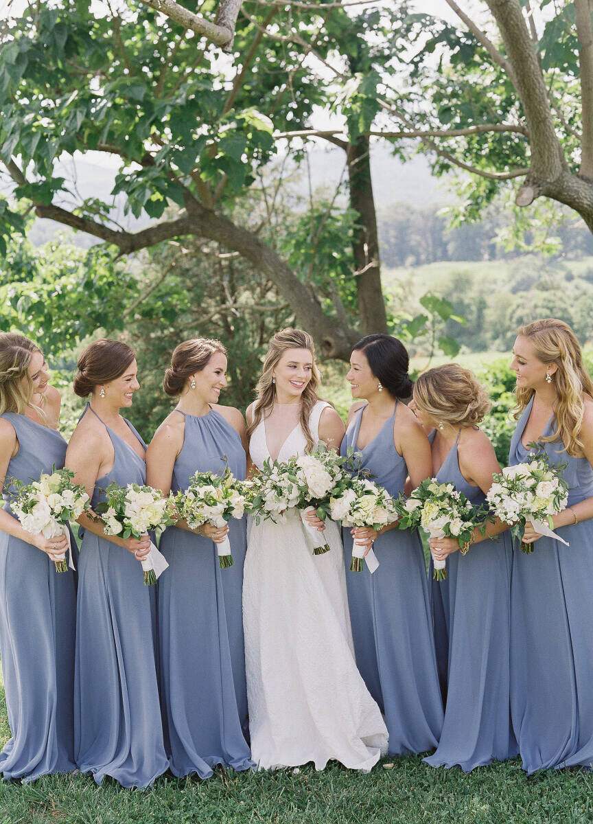 Wedding Website Examples: A bride posing with her six bridesmaids, who are all dressed in slate blue.