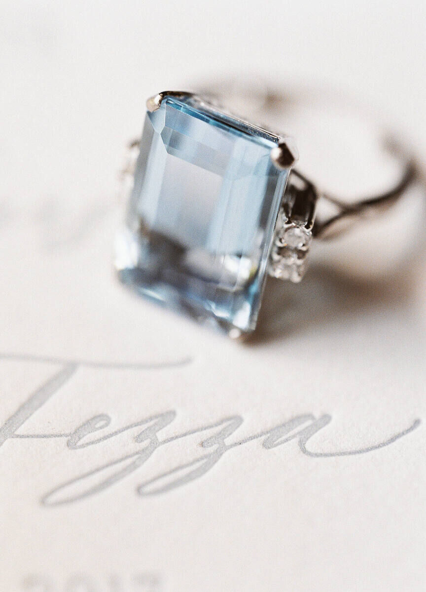 Wedding Website Examples: A close-up of a light blue -jeweled engagement ring on top of a wedding invitation.