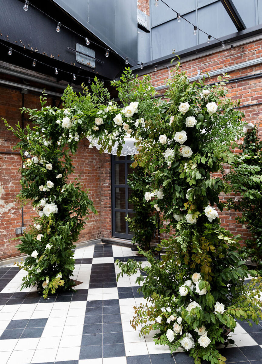 Wedding Website Examples: A wedding arch with greenery and white florals in an industrial wedding ceremony venue.