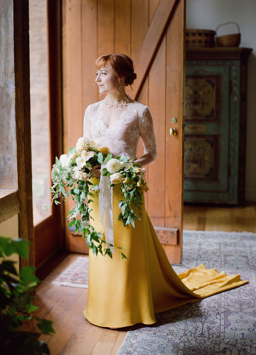 Wedding Website Examples: A bride wearing a white and marigold color-blocked wedding gown and holding her bouquet of white florals.