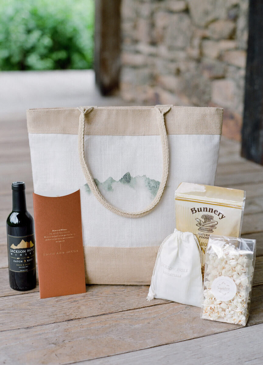 Wedding Website Examples: An arrangement of welcome bag essentials including a bottle of wine, itinerary, popcorn and more.