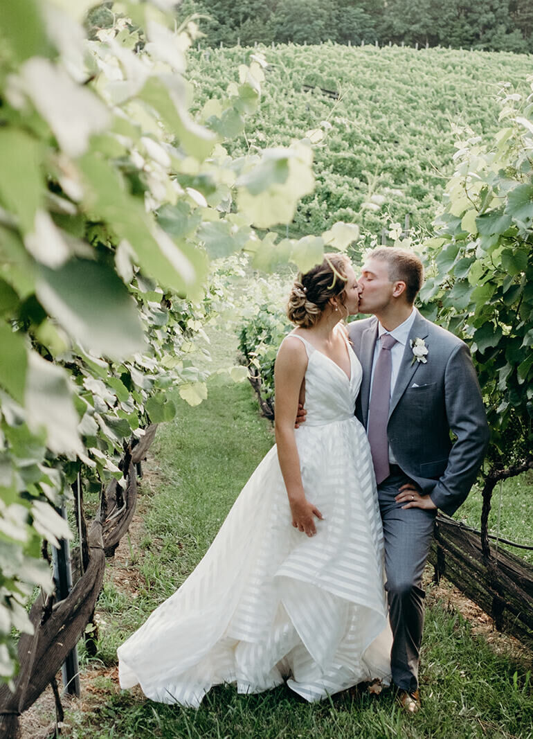 Wedding Website Examples: A wedding couple sharing a kiss in the middle of a vineyard.