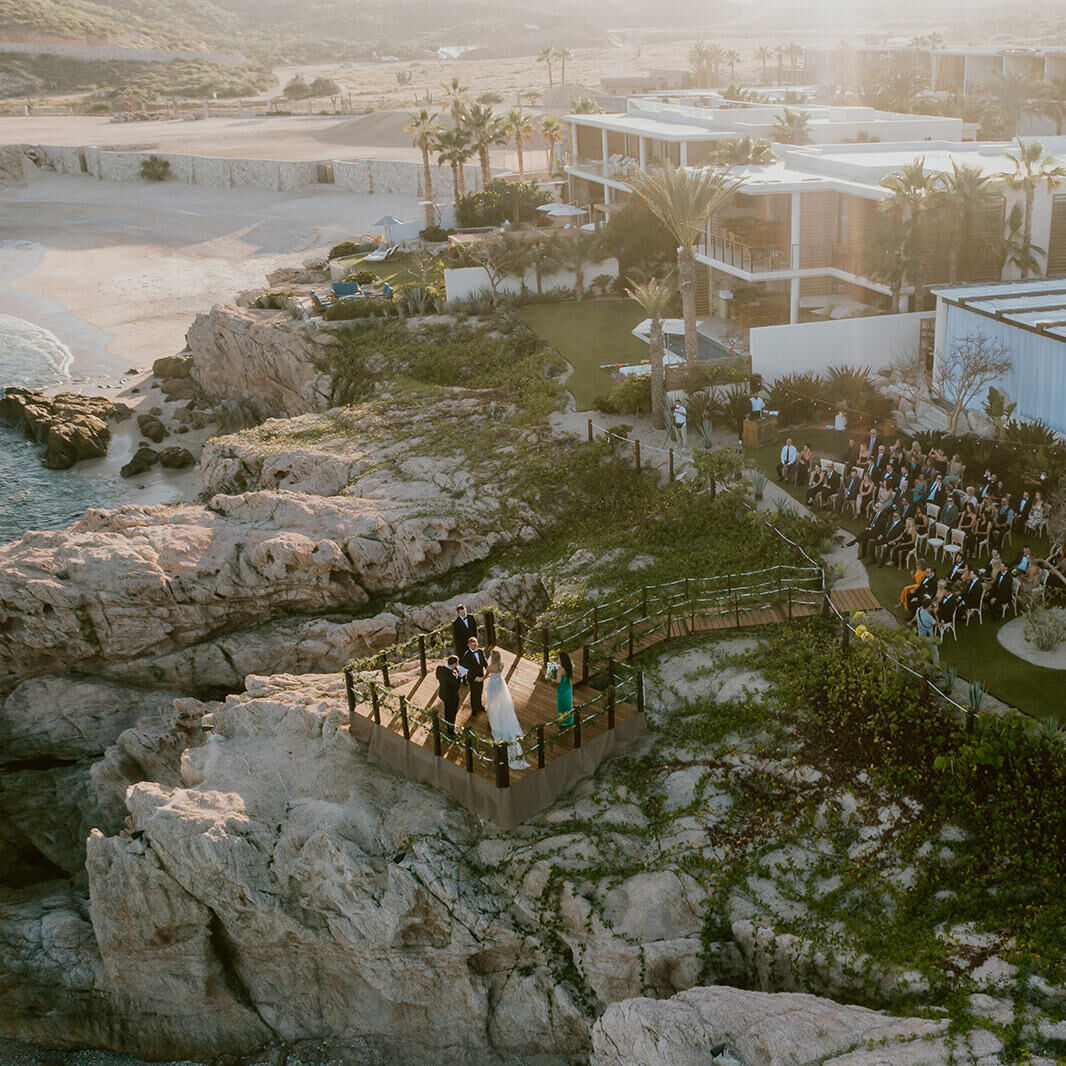 A drone photograph of a couple getting married on a beachfront platform at their Chileno Bay Resort wedding in Cabo.